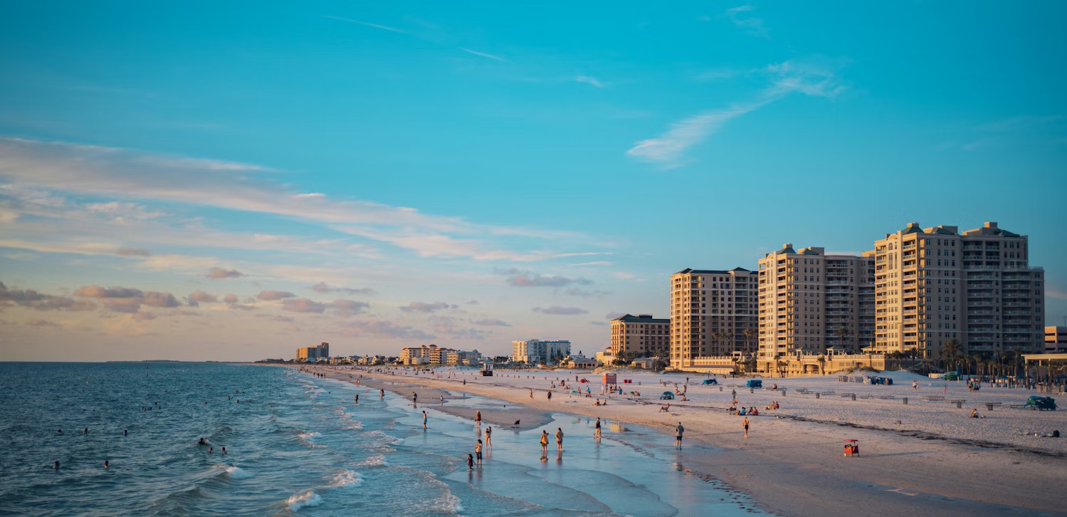 A view of soft white sands with a vibrant turquoise sky, meeting the gentle Gulf waves as visitors enjoy the warm Florida sunset along the iconic coastline.