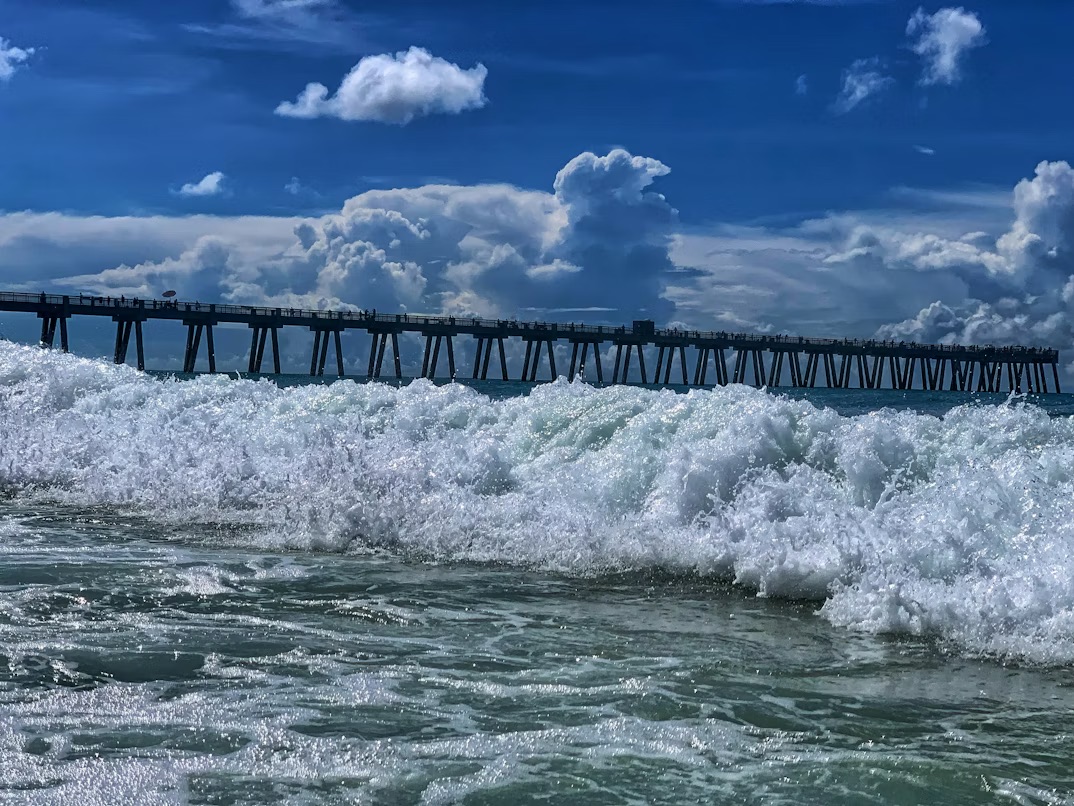Alongside the waves of the beach's ocean, lays a visible view of the Navarre Pier in the background.